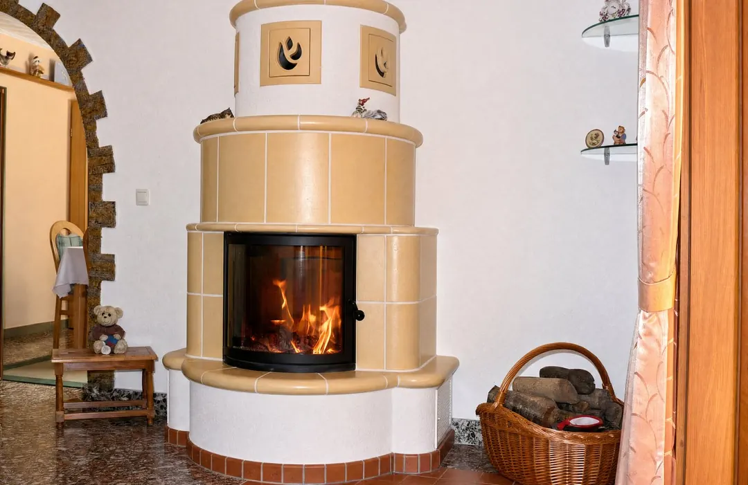 Runder Ofen mit Ornamentkacheln in einem Wohnraum mit Holzkorb